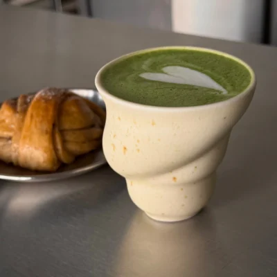 Skal kop med grøn matcha og wienerbrød på en håndlavet, hvid keramikskål med brune pletter.